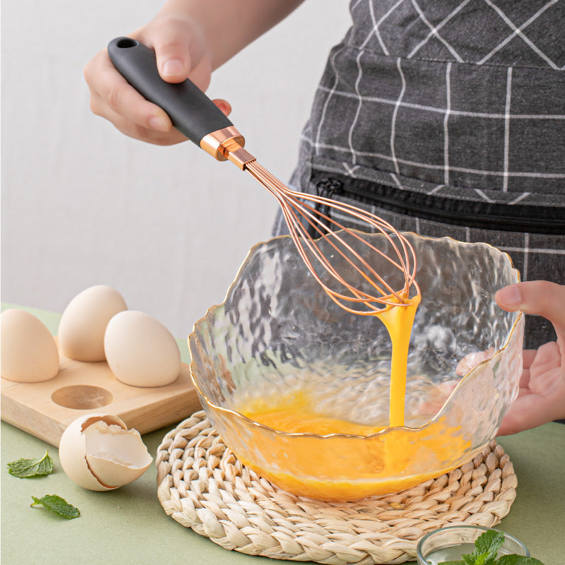 Whisking eggs in a glass bowl with a copper-plated kitchen tool from the Rose Gold Kitchen Household Peeler Gadget Copper Plating Set.