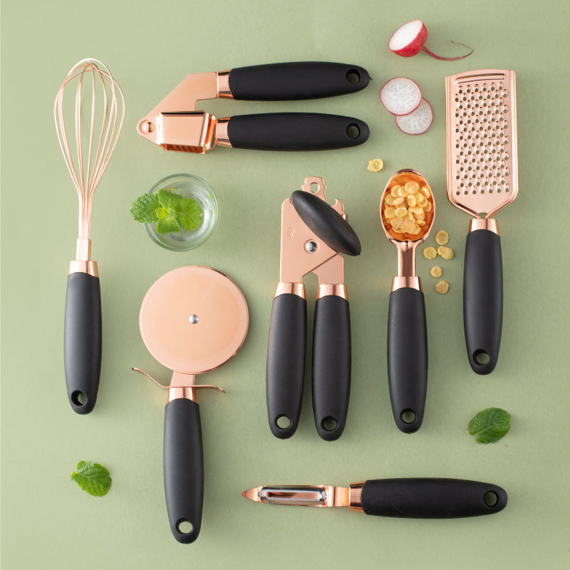Rose gold kitchen tool set with copper plating, including peeler, whisk, grater, pizza cutter, and more, displayed on a countertop.